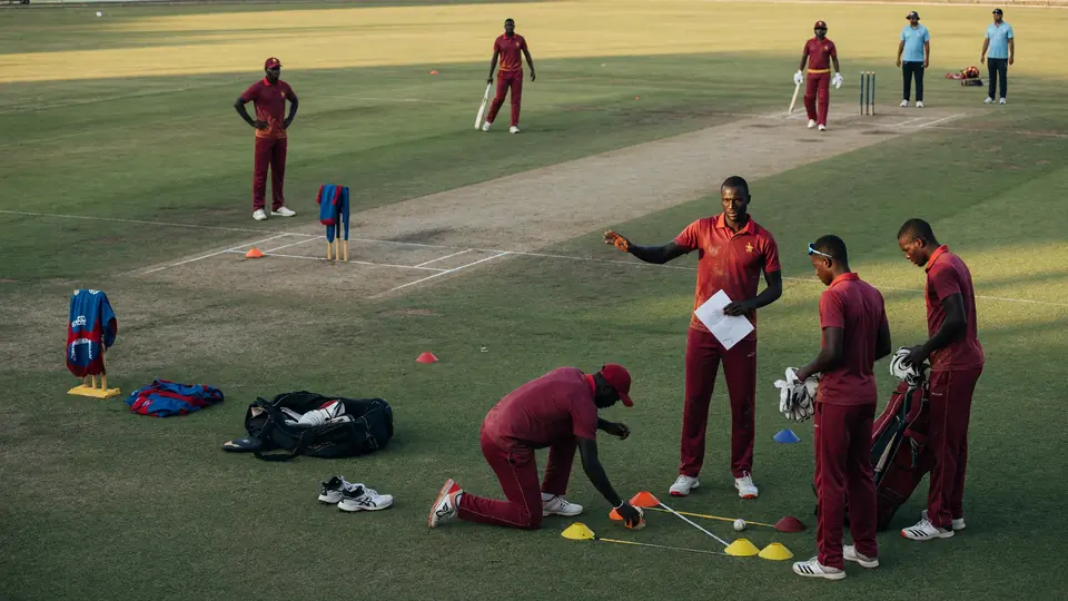 Maroon-kit players setting orange cones on a practice pitch while teammates wait near the crease